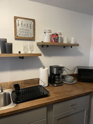 A kitchen with a wooden countertop, a coffee maker, a microwave, and a sign that reads "this home with love & laughter".