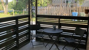 Een overdekt terras met een tafel en stoelen, een houten omheining en uitzicht op een huis en bomen.