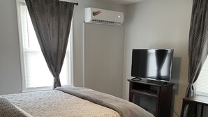 Een slaapkamer met een bed, een televisie op een standaard, een airconditioning en een plafondventilator.