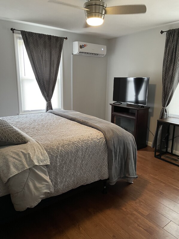 A bedroom with a bed, a television on a stand, an air conditioning unit, and a ceiling fan.