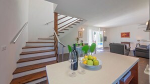 A modern kitchen with a central island, a dining area with green chairs, and a staircase leading to another level.