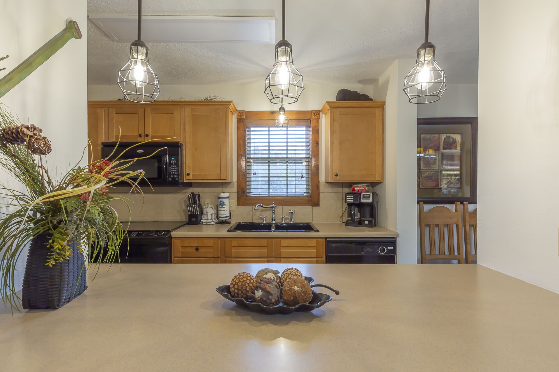 Une cuisine avec des meubles en bois, un îlot central agrémenté d’un récipient contenant des objets décoratifs, un four à micro-ondes et des luminaires suspendus.