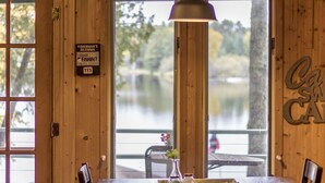 Un intérieur en bois avec une table et des chaises, un panneau indiquant un endroit où pêcher, et une vue sur un lac à l’extérieur.