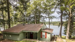 Une petite cabane à l’extérieur vert, avec une cheminée et une vue sur un lac.