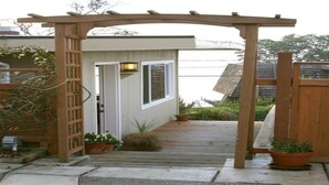Une terrasse en bois mène à une maison à l’extérieur blanc, dotée d’un petit porche.