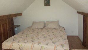 A small, cozy attic bedroom with a sloped ceiling, a wooden headboard, a bed with a floral-patterned bedspread, and a single wall-mounted painting. - Willow apartment at Kamenný potok (Kájov)