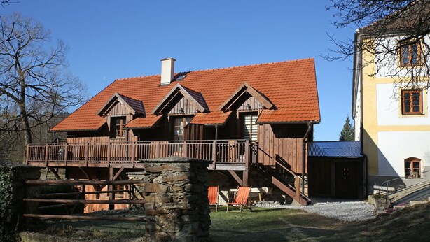 A wooden house with a red roof, a balcony, and a stone structure in front. - Willow apartment at Kamenný potok (Kájov)