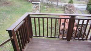 A wooden deck with a metal railing, overlooking a grassy area with a stone wall and a road in the background. - Willow apartment at Kamenný potok (Kájov)