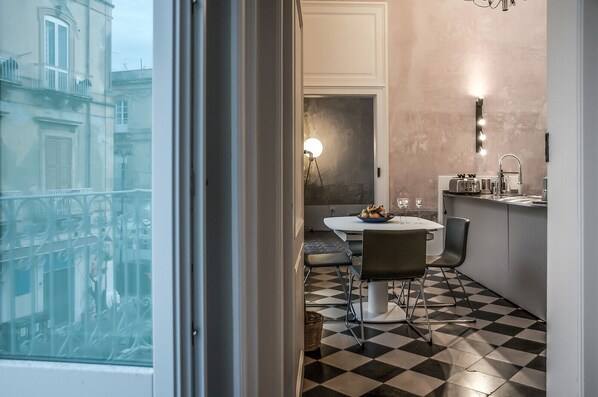 A modern kitchen with a checkered floor, a dining table with chairs, a sink, and a countertop with a toaster and other appliances. - Stylish apartment overlooking the historic market of Ortigia (siracusa)