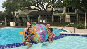 Una piscina con borde de azulejos, una pelota inflable grande y una persona con traje de baño estampado.