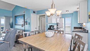 Un comedor con una mesa y sillas de madera, una araña y vista a la cocina.