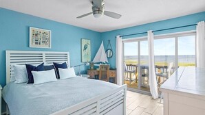 Un dormitorio con cama, ventilador de techo, escritorio y vistas al exterior.