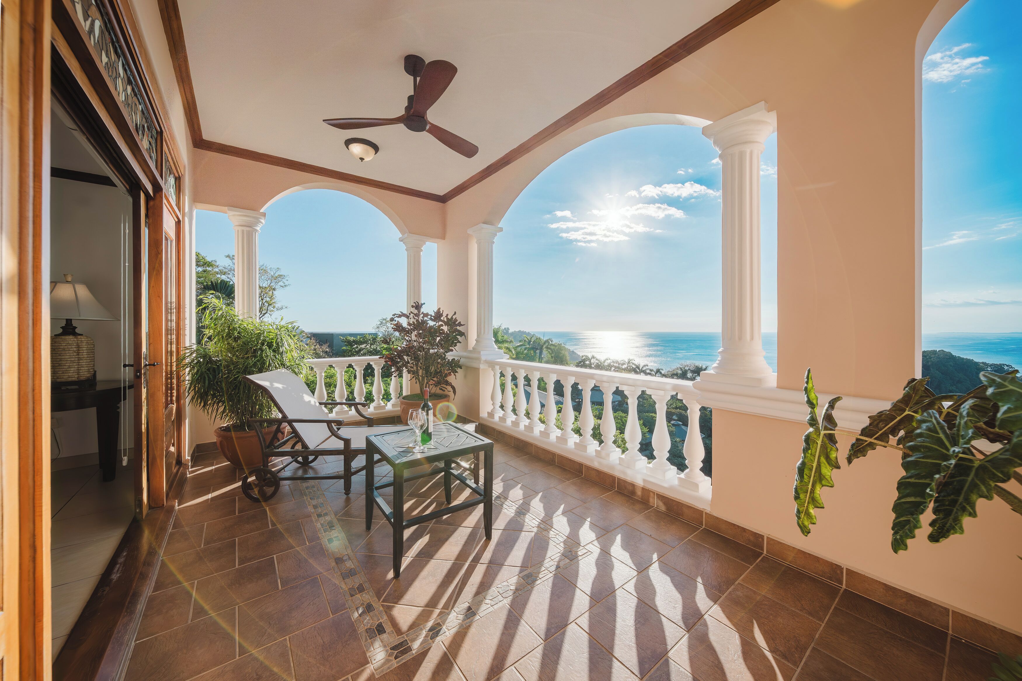 Un balcón con vista al mar, un ventilador de techo y plantas en macetas.