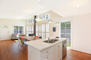 A modern kitchen with a central island, built-in appliances, and large windows. - 24A Petrel Ave - Wi-Fi (Encounter Bay)