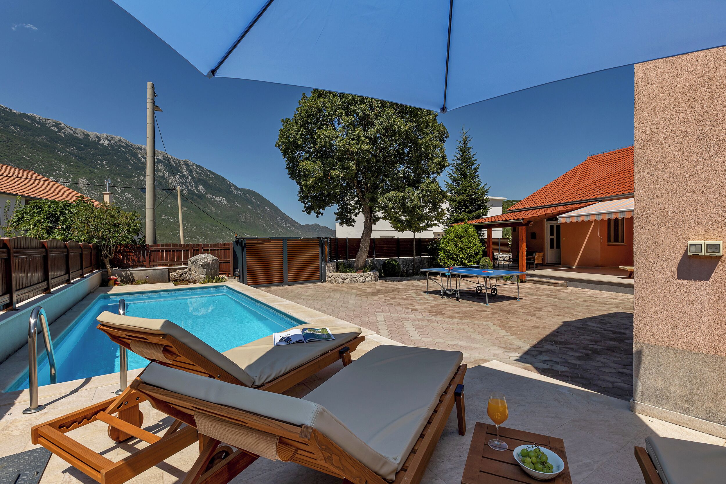 A poolside area with lounge chairs, a table with a drink, and a view of mountains.