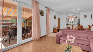 A living room with a sofa, a dining area with chairs, a kitchen area, and a sliding glass door leading to an outdoor space.