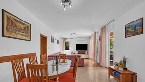 A dining area with a round table and chairs, a sofa, a TV, and a window with curtains.