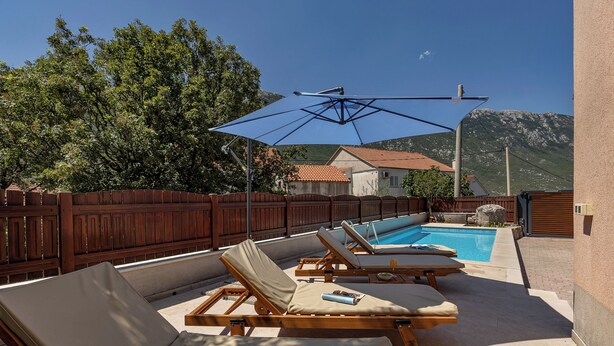 A poolside area with lounge chairs, a blue umbrella, and a mountain view.