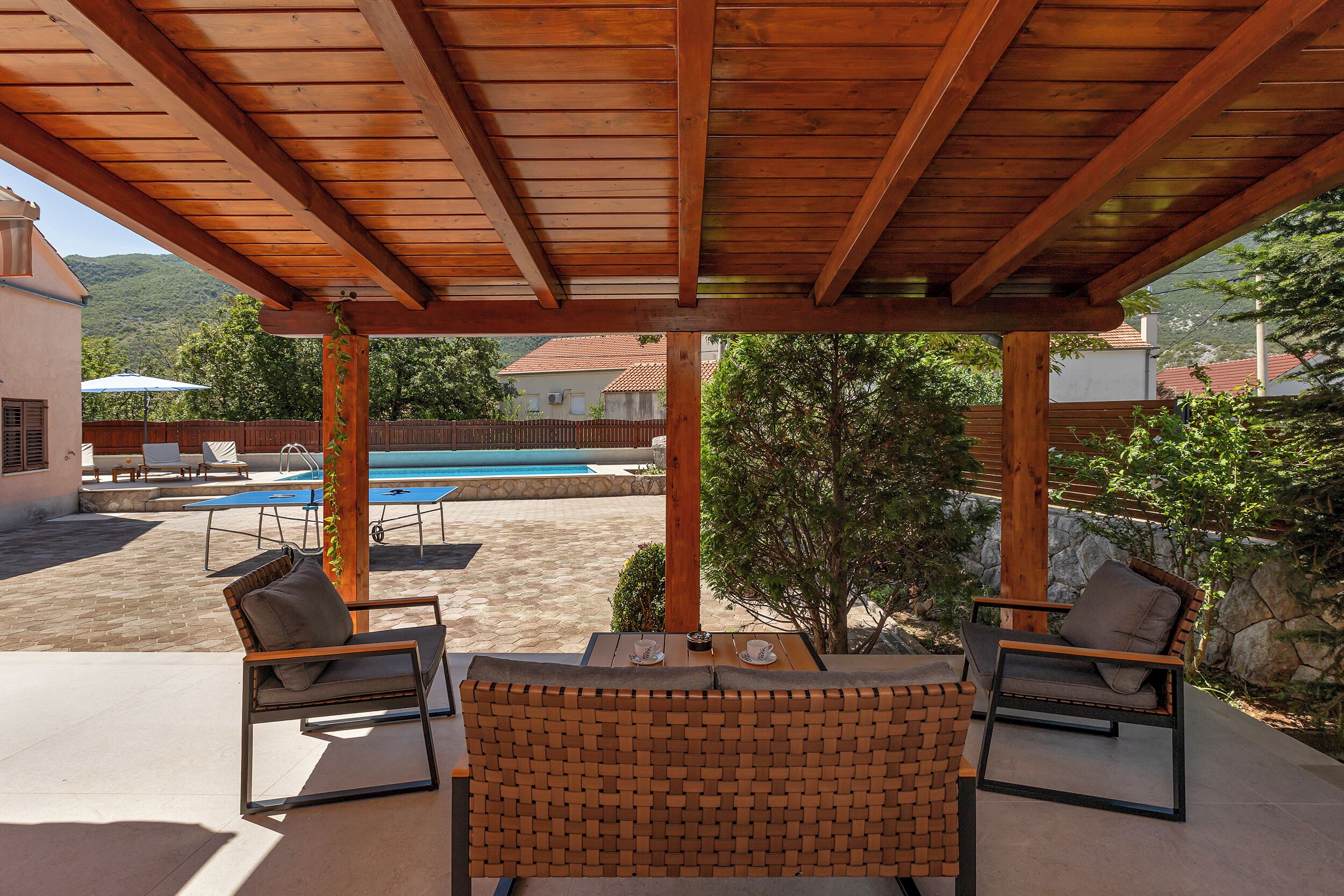 Un espace extérieur aménagé avec des sièges, protégé du soleil, et une piscine en arrière-plan.