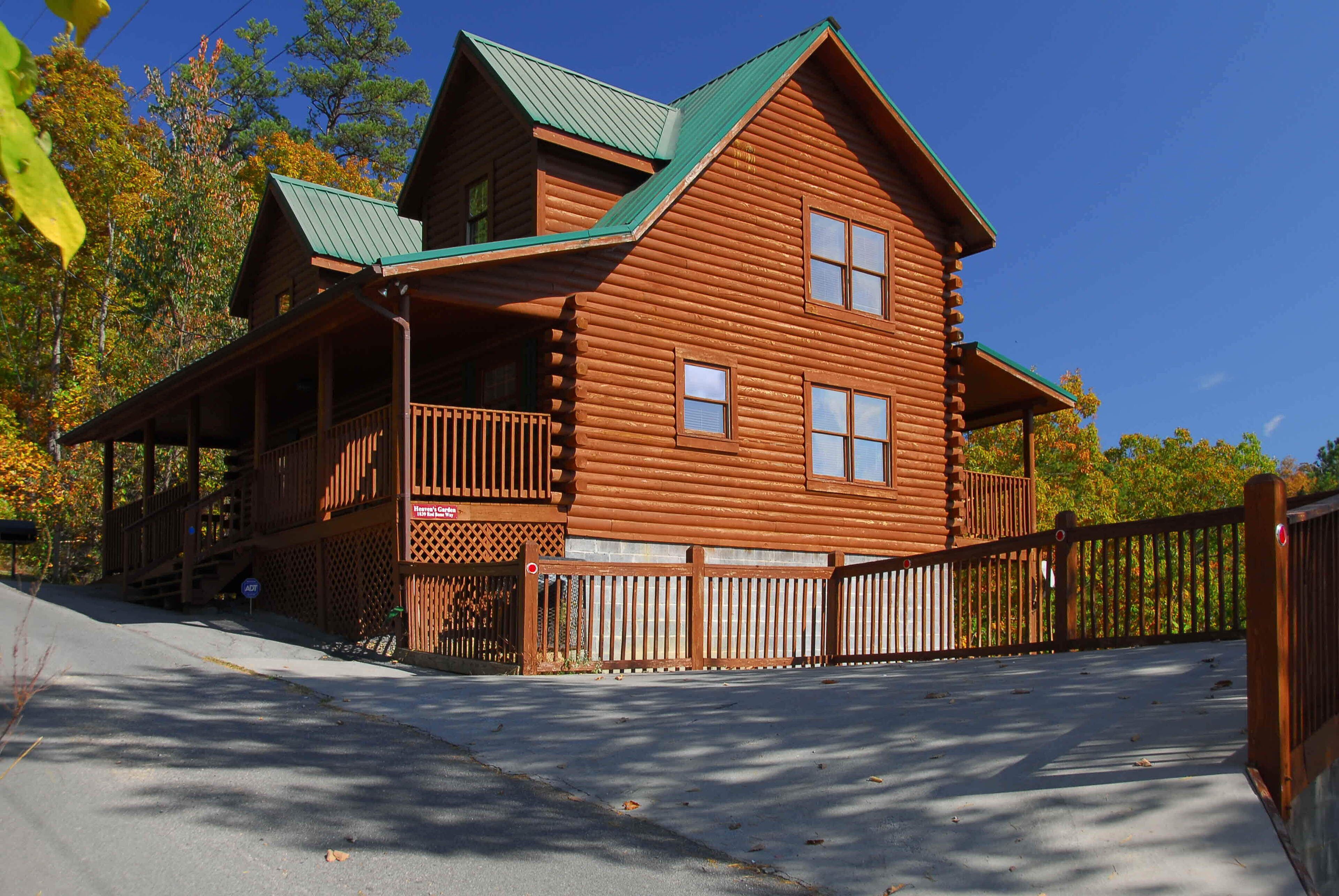 A log cabin with a porch and a green roof, surrounded by a wooden fence.