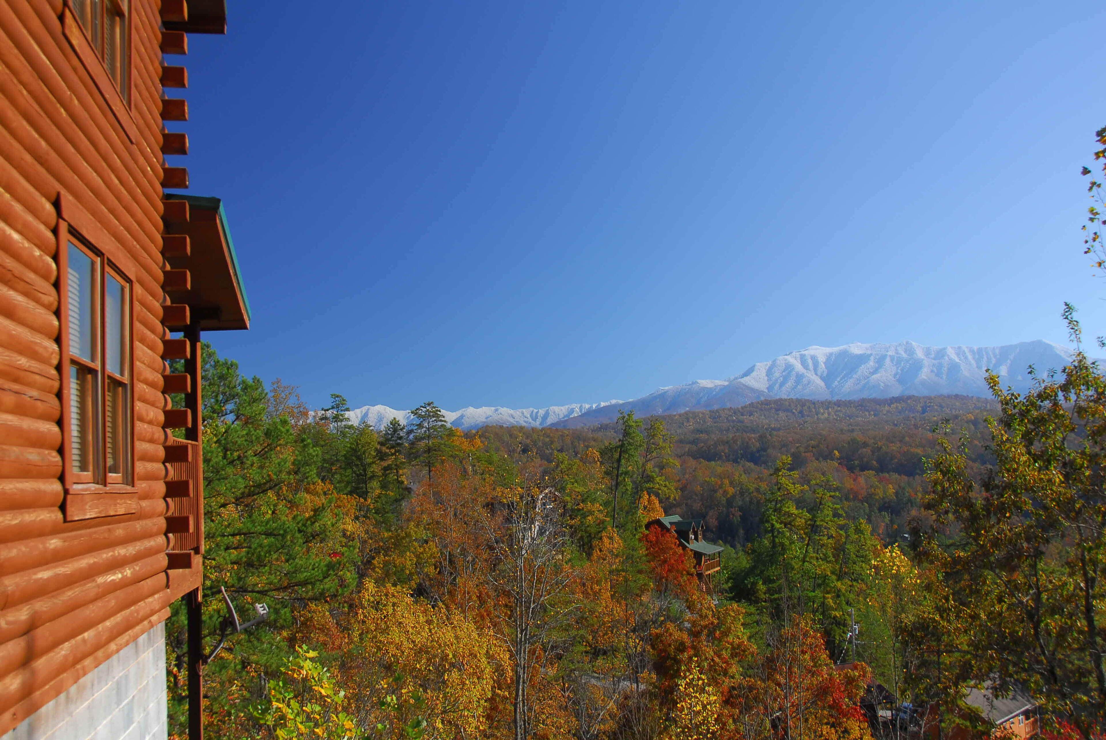 Una cabana de fusta amb vista a muntanyes nevades i fullatge d'octubre.