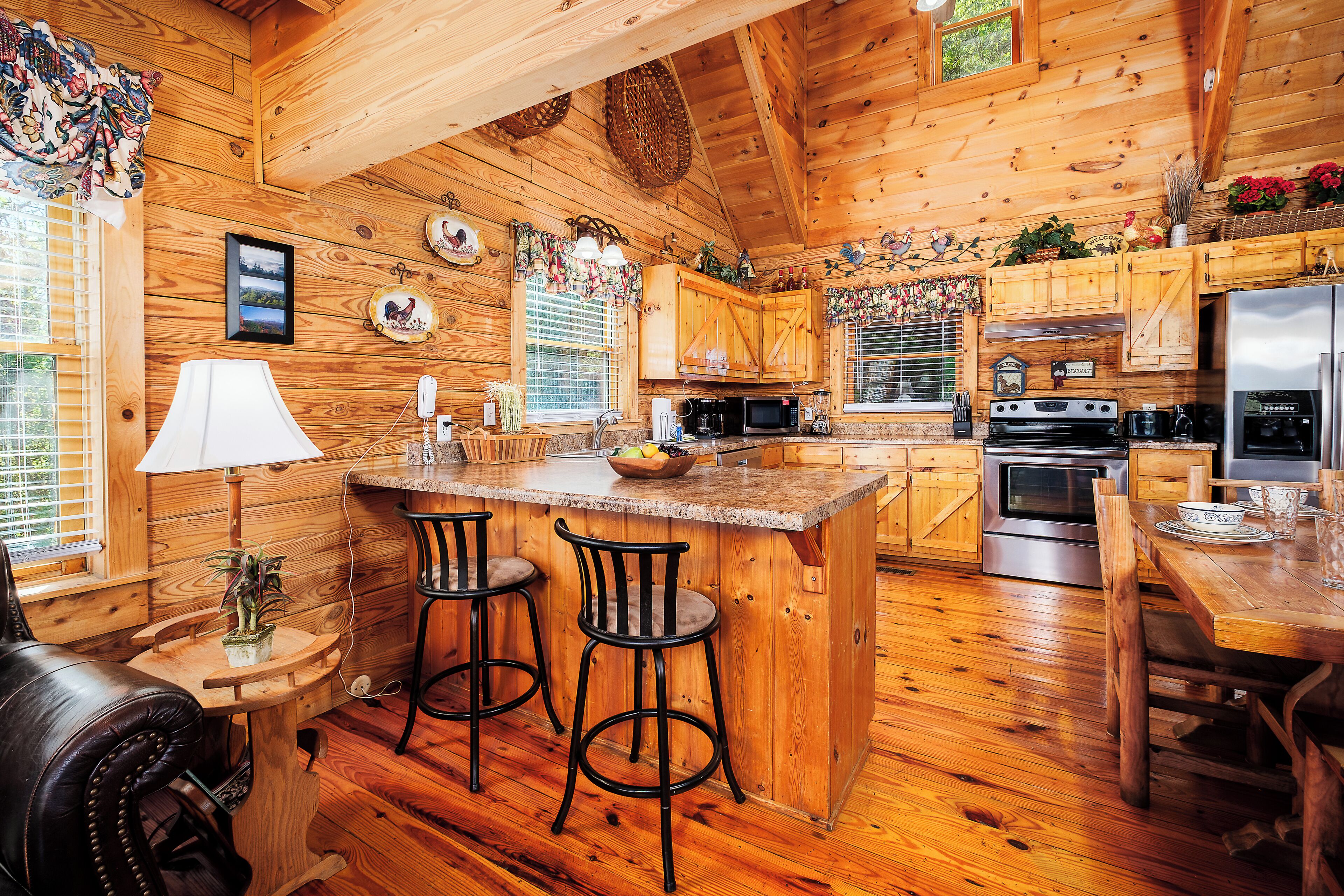 A wooden cabin interior with a kitchen featuring a central island, bar stools, and a dining table.