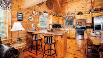 A wooden cabin interior with a kitchen featuring a central island, bar stools, and a dining table.