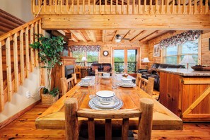 A wooden cabin interior with a dining area, a sofa, and a view through the windows. - 🏔️ Heaven's Garden🌲Mt LeConte Views, HotTub, near Dollywood (Sevierville)