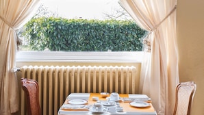 Un coin repas avec une table dressée pour deux personnes, un lustre et une fenêtre avec des rideaux.