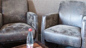 Une pièce comprenant deux fauteuils en cuir, une table basse en bois avec une bouteille et des verres, et un téléviseur à écran plat fixé au mur.