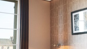 Une chambre d’hôtel avec un lit, une fenêtre, une lampe fixée au mur et un tableau encadré.