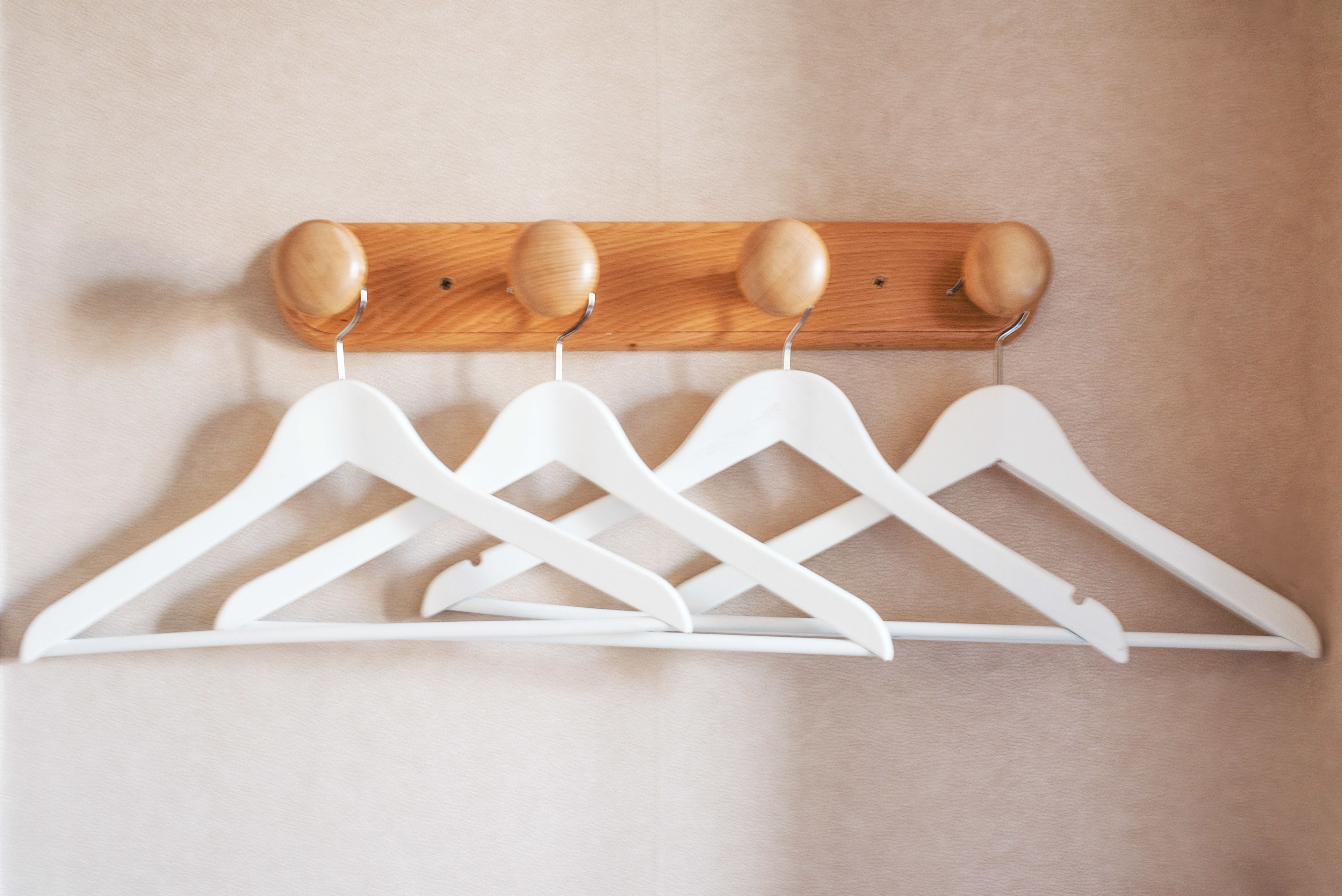 Un perchero de madera con cuatro perchas blancas frente a una pared color crema.