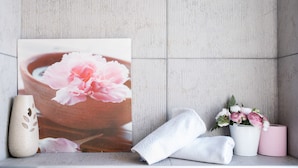 Une salle de bain décorée d’un grand motif floral, avec un vase, une serviette et une bougie rose.