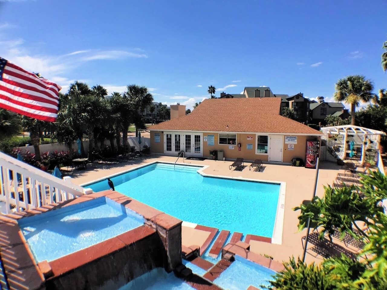 A swimming pool with a red-tiled deck, lounge chairs, and a palm tree in the background.