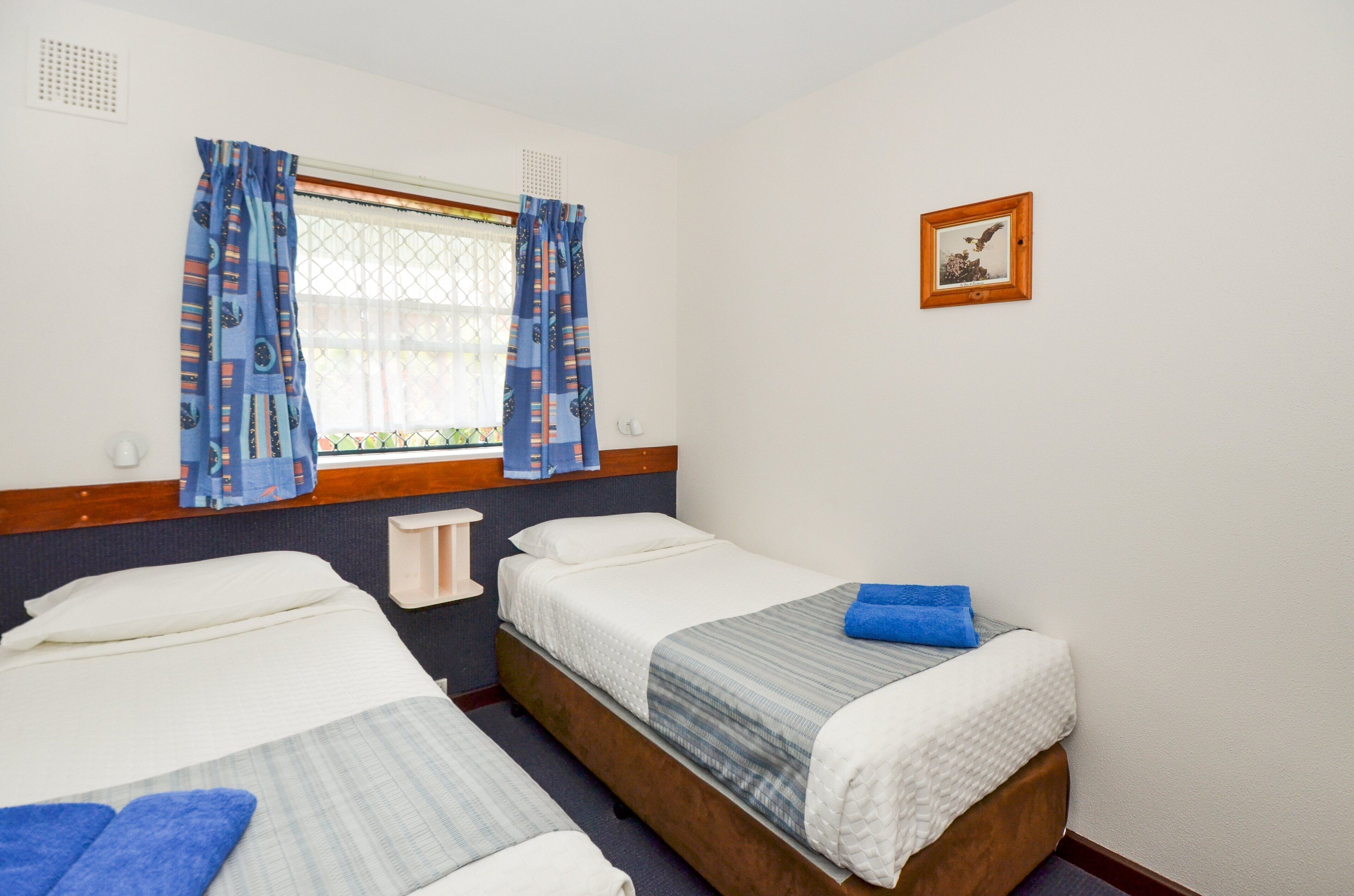 Habitación de hotel con dos camas, una ventana con cortinas, un cuadro en la pared y una mesita de noche.