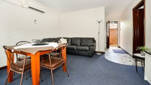 A compact living space with a dining table, chairs, a black leather sofa, a standing lamp, and a small table with a plant. - SELF CONTAINED-1 Bdrm Apartments (Albany)