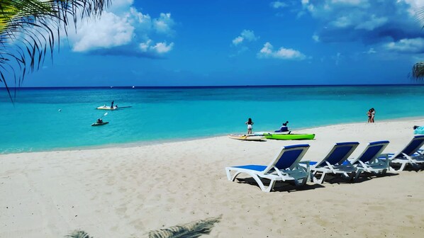 Una playa con agua turquesa cristalina, kayaks y sillones de playa.
