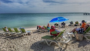 A beach with rows of sun loungers and umbrellas, a clear view of the ocean, and a pier in the distance. - Outstanding pool and outdoor area 5 minute walk to beach! (Marathon)