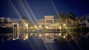 A waterfront property with a reflective pool, a boat dock, and a well-lit building with multiple levels. - Outstanding pool and outdoor area 5 minute walk to beach! (Marathon)