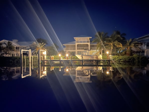 A waterfront property with a reflective pool, a boat dock, and a well-lit building with multiple levels.
