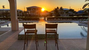 A sunset view from a poolside area with two chairs facing the water, a building with a balcony, and a clear sky. - Outstanding pool and outdoor area 5 minute walk to beach! (Marathon)
