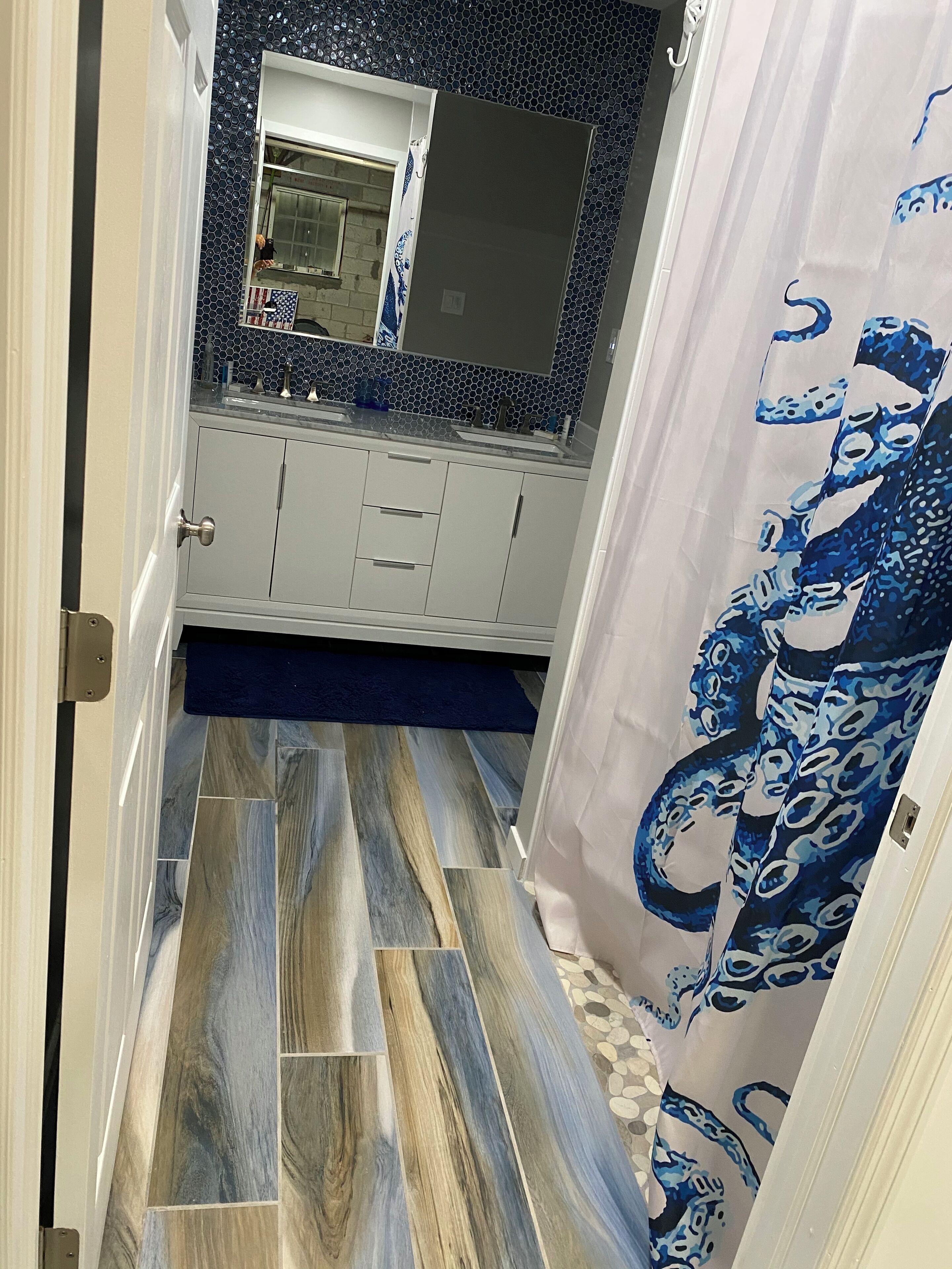 A narrow hallway with a tiled floor, a white door, and a bathroom with a mirror, sink, and tiled backsplash.
