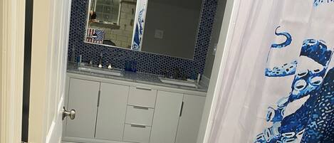 A narrow hallway with a tiled floor, a white door, and a bathroom with a mirror, sink, and tiled backsplash.