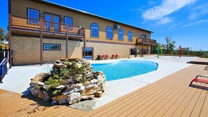 Un edificio a due piani con piscina, terrazza in legno e area relax all'aperto.