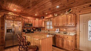 A wooden cabin-style kitchen with a central island, bar stools, wooden cabinets, a stainless steel refrigerator, a microwave, and a sink. - A Home For The Starrs: Spectacular Views! Resort Pool. Got it all. Near Dollywood and Pigeon Forge! (Sevierville)
