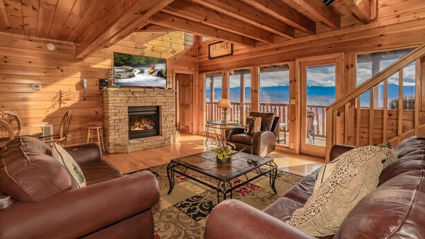 A cozy log cabin interior with a fireplace, leather sofas, a coffee table, and a TV mounted on the wall. - A Home For The Starrs: Spectacular Views! Resort Pool. Got it all. Near Dollywood and Pigeon Forge! (Sevierville)