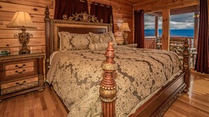 A wooden cabin bedroom with a large bed, two bedside tables with lamps, a dresser, and a balcony with a view. - A Home For The Starrs: Spectacular Views! Resort Pool. Got it all. Near Dollywood and Pigeon Forge! (Sevierville)