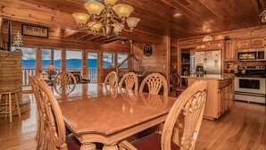 A wooden dining room with a large table and chairs, a chandelier, and a view of mountains through large windows. - A Home For The Starrs: Spectacular Views! Resort Pool. Got it all. Near Dollywood and Pigeon Forge! (Sevierville)