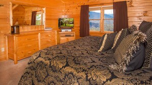 Ein Schlafzimmer in einer Blockhütte mit einem großen Bett, einem Schminktisch, einem Fernseher und einem Fenster mit Blick auf die Berge.