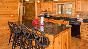 Ein Holzblockhaus-Interieur mit einer Küche, die eine zentrale Kochinsel, Barhocker und Pendelleuchten beinhaltet.